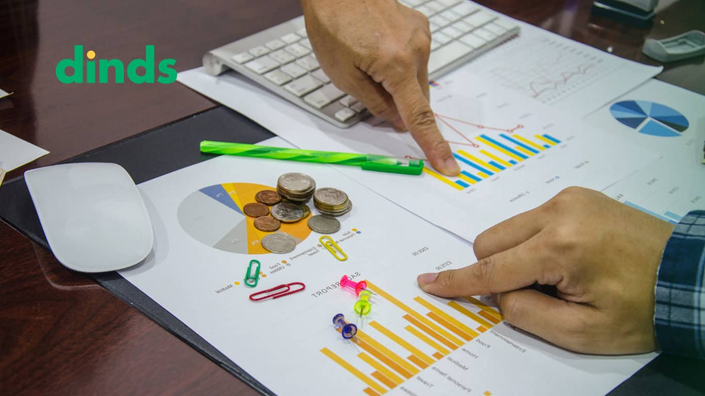 duas maõs apontam gráficos em papéis com moedas em cima