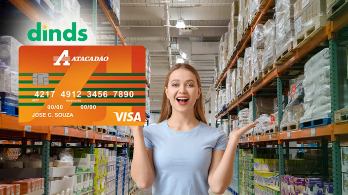 mulher sorri e mostra prateleiras de mercado com cartão atacadão ao lado