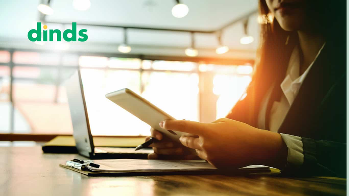 mulher segura e olha para tela de tablet com notebook aberto na mesa