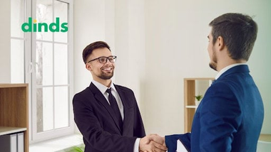 dois homens de negócios apertando as mãos após negociação de crédito imobiliário com logo do Dinds visível ao fundo