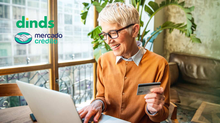 mulher sorri segurando cartão de crédito e digitando em notebook
