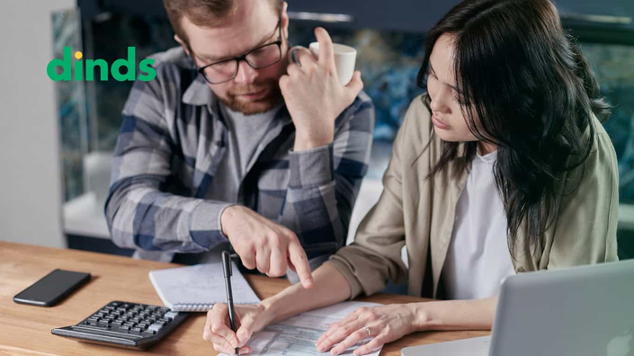 casal escreve e olha para papéis com calculadora e notebook na mesa