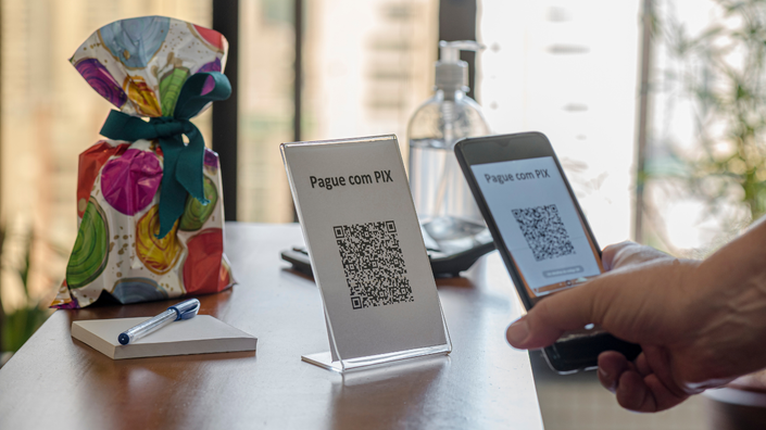 imagem com qr code sobre a mesa e um celular apontando para ele para poder realizar o pagamento via pix
