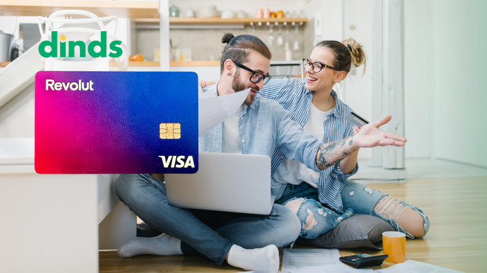 casal sorri sentados no chão segurando papéis e cartão de crédito com notebook aberto