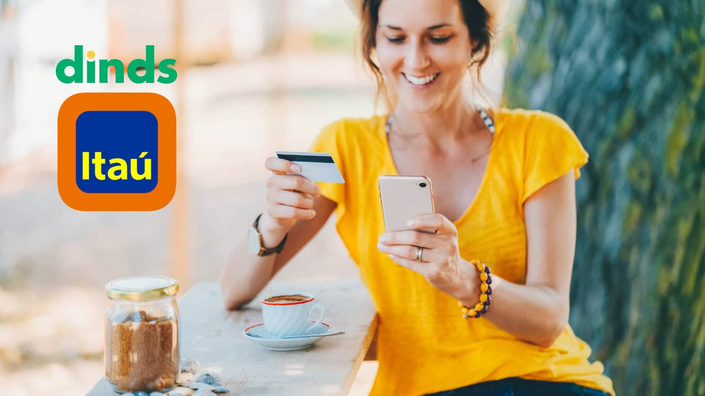 mulher sorri segurando celular e cartão com xícara na mesa
