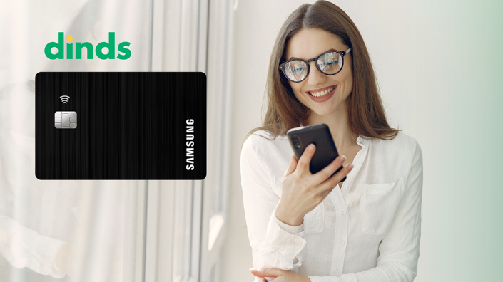 mulher sorri olhando para tela do celular que segura na mão com cartão samsung ao lado