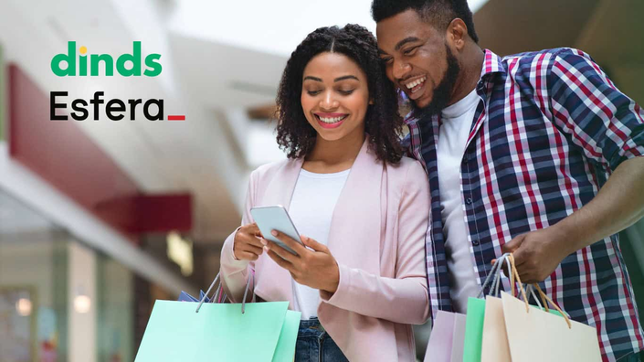 casal olha feliz para tela de celular segurando sacolas de compras