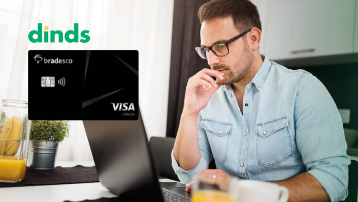 Homem no computador com cartão de crédito bradesco visa infinite ao lado