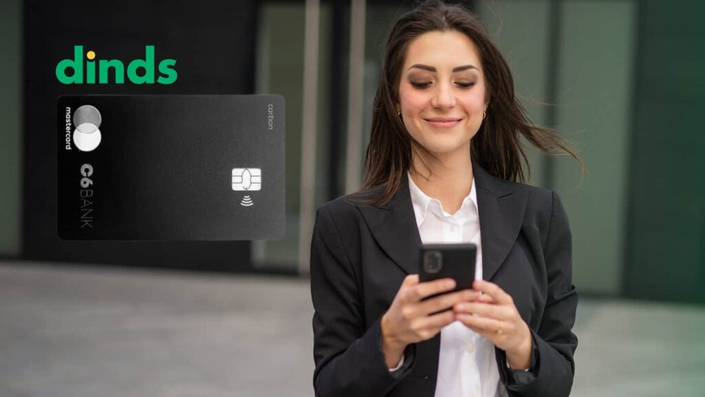 Mulher sorrindo com celular na mão e cartão de crédito c6 carbon ao lado