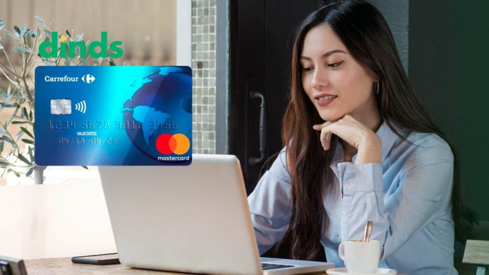 Mulher sorrindo no computador com Cartão de crédito carrefour ao lado