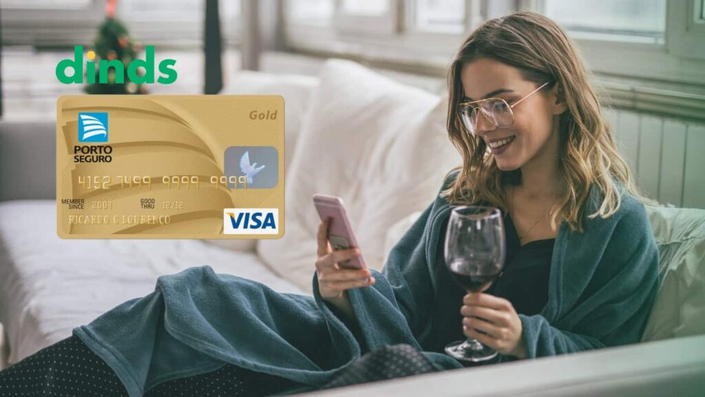 Mulher com celular na mão e taça, com cartão de crédito porto seguro gold ao lado