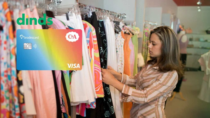 Mulher em loja de roupas com o cartão de crédito C&A ao lado.