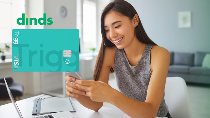 mulher sorrindo mexe no ceular com notebook baerto e com cartão trigg ao lado