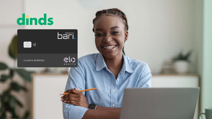 Mulher sorrindo na frente do computador com cartão de crédito Banco Bari ao lado