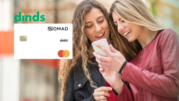 Duas mulheres olhando para o celular sorrindo com cartão de débito nomad ao lado