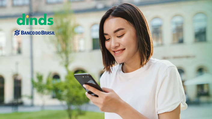 Mulher sorrindo com celular na mão e empréstimos banco do brasil ao lado