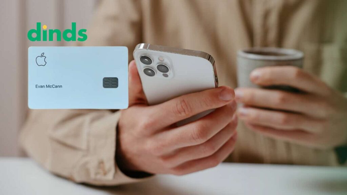 Pessoa segurando iPhone e xícara de café ao lado da imagem do Apple Card e logo do Dinds.