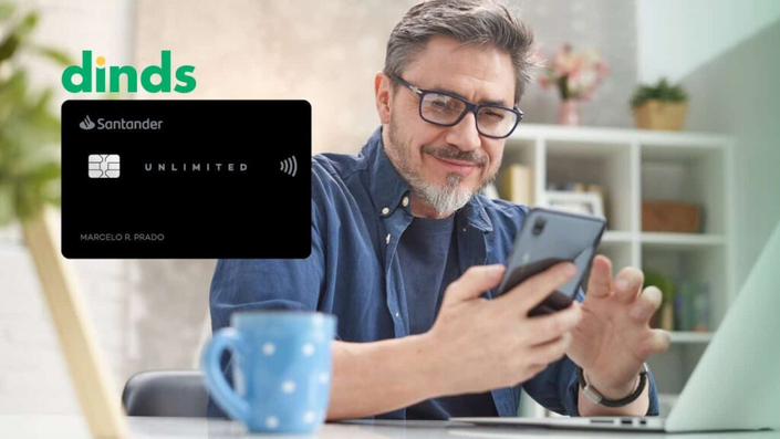 Homem sorrindo para o celular com cartão de crédito santander unlimited