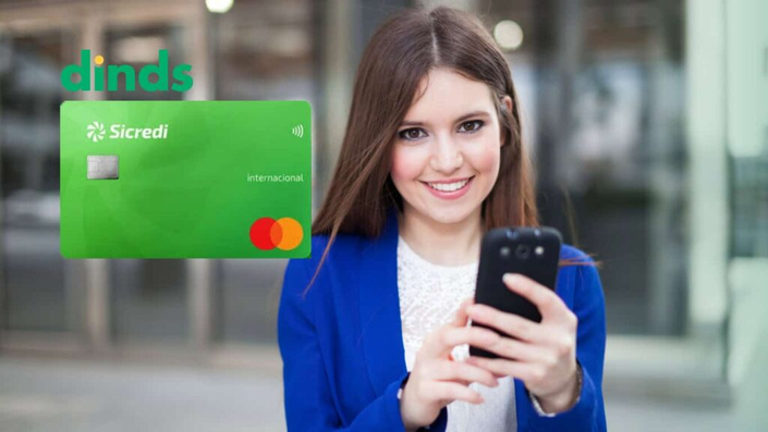 Mulher sorrindo com celular na mão, cartão de crédito sicredi internacional ao lado