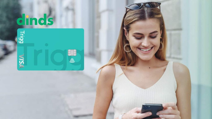 Mulher sorrindo com celular na mão e cartão trigg ao lado
