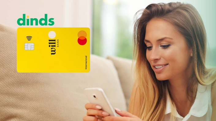 Mulher sorrindo com celular na mão e cartão de crédito will bank ao lado